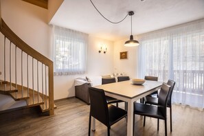 A dining area with a wooden table, black chairs, a light fixture, and a staircase.