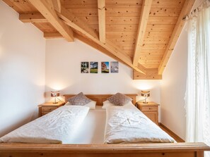 Un lit double avec deux tables de chevet, des poutres en bois au plafond et trois tableaux encadrés accrochés au mur.
