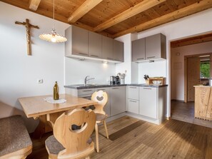 A modern kitchen with wooden beams, a dining table with chairs, and a cross on the wall.