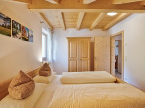 Quarto com duas camas, vigas de madeira no teto, guarda-roupa e janela com cortinas.