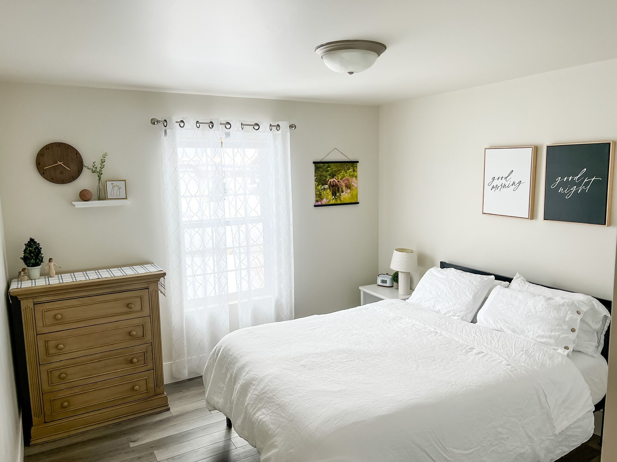 A bedroom with a bed, dresser, bedside table, and wall decorations.