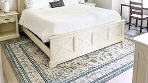 Una camera da letto ordinata con un letto, comodini, un ventilatore a soffitto, un quadro incorniciato e un tappeto decorato.
