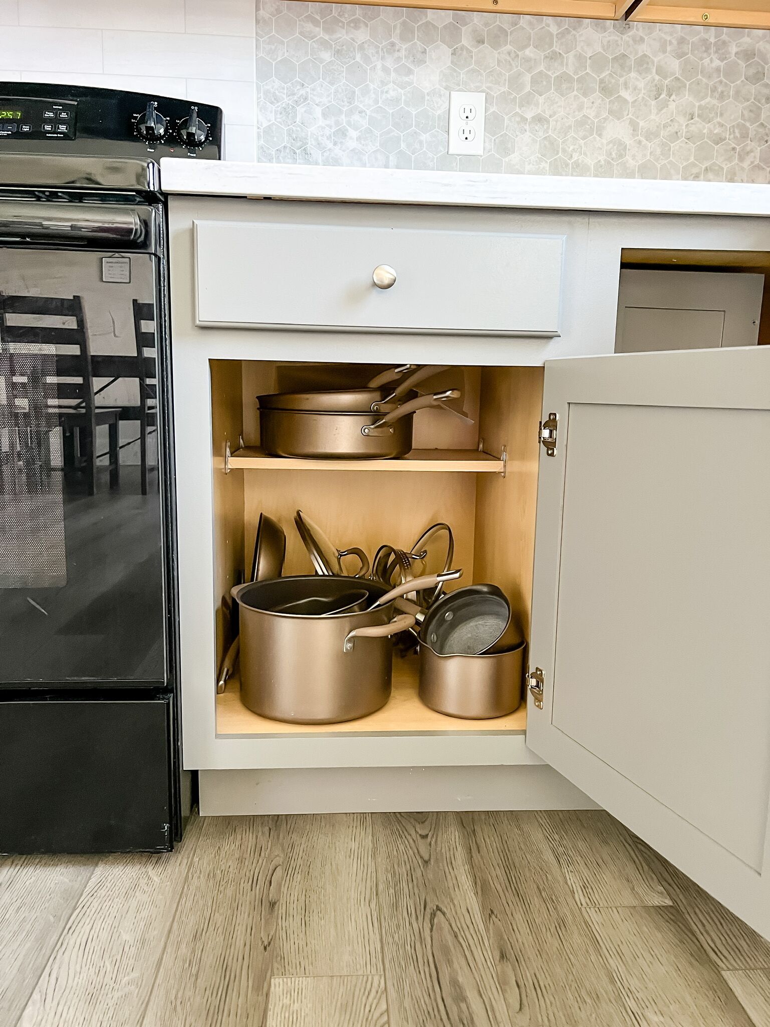 A kitchen with a built-in oven, a microwave, and a cabinet with pots and pans.