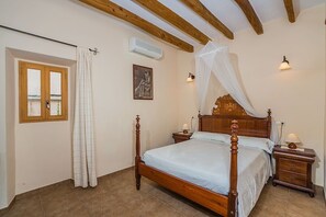 Ein Schlafzimmer mit einem hölzernen Himmelbett, einem Fenster mit Vorhängen, einer Klimaanlage, einem Nachttisch mit Lampe sowie einer Wandleuchte.