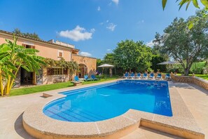 Ein Swimmingpool mit Liegestühlen, einer Steinmauer und einem Gebäude mit Ziegeldach.