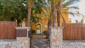 Una puerta de piedra que da a un edificio con puerta de madera, rodeado de palmeras y una valla.