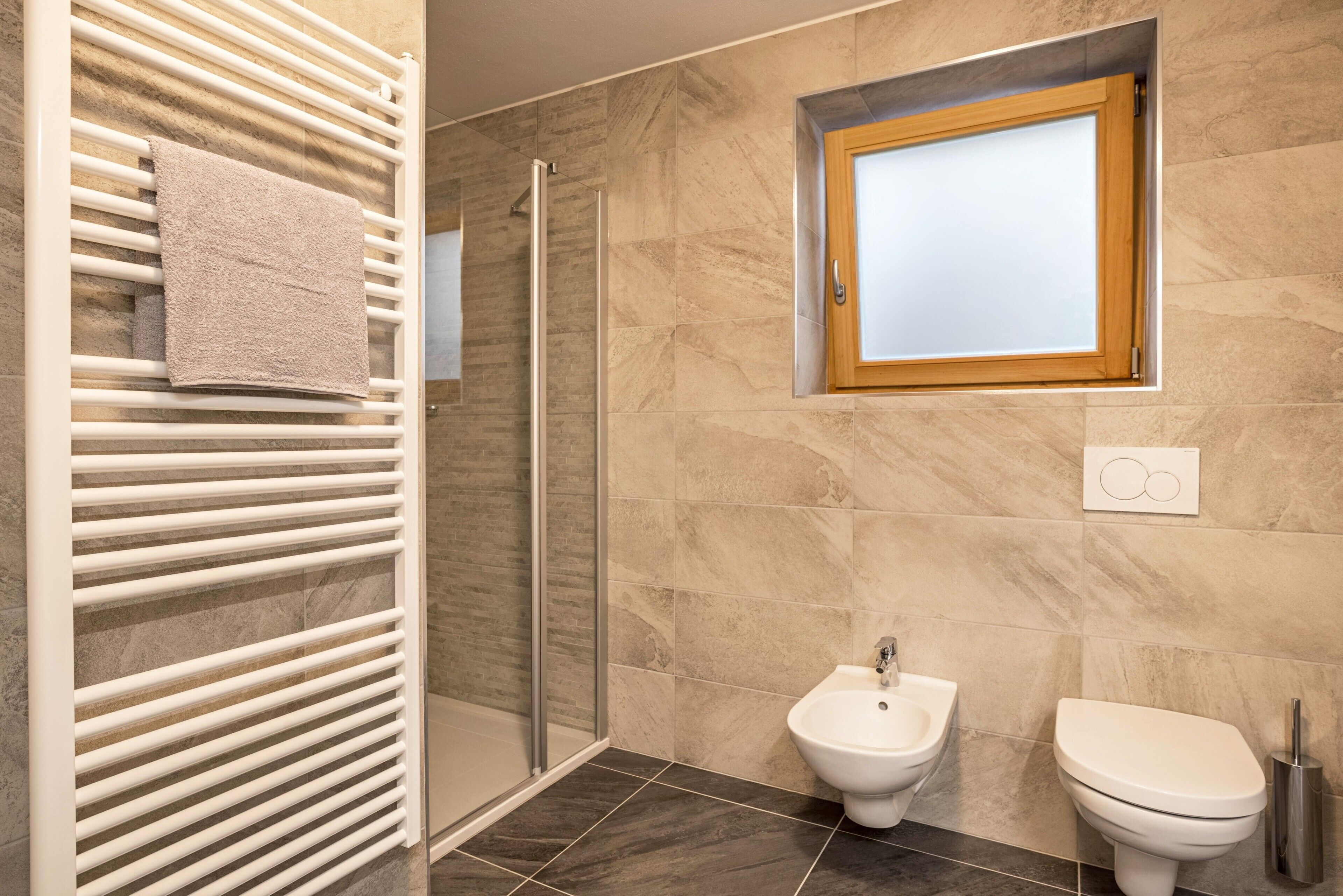 Un bagno moderno con cabina doccia in vetro, termosifone bianco, bidet e water.