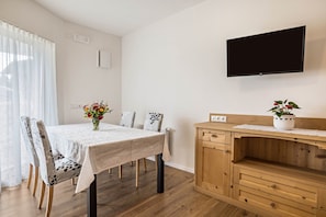 A dining area with a table, chairs, a TV mounted on the wall, and a wooden cabinet with drawers.