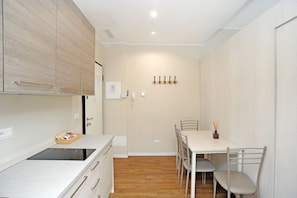 Une cuisine moderne avec un coin repas, un plancher en bois et un mur blanc agrémenté d’un porte-manteau.