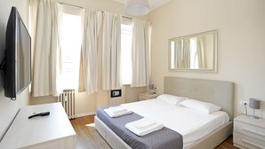 Ein Hotelzimmer mit einem Bett, einem Fernseher, einem Schreibtisch, einer Lampe und einem fenster mit Vorhängen.