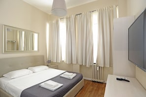Une chambre d’hôtel avec un lit, une télévision, un miroir et une fenêtre avec des rideaux.