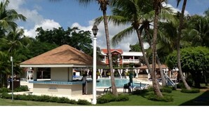 Een resort met een zwembad, palmbomen en een gebouw met een rood dak.