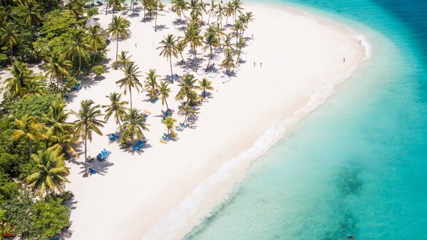 Luchtbeeld van een strand met wit zand, helder turquoise water en palmbomen.