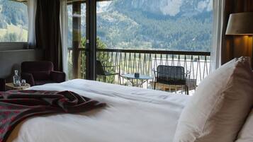 Ein Hotelzimmer mit einem großen Bett, einem Balkon mit Bergblick und einem Tisch mit Stühlen.