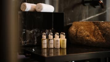 Une salle de bain avec un comptoir noir, quatre flacons de produits de toilette, une serviette et un grand lavabo en pierre.