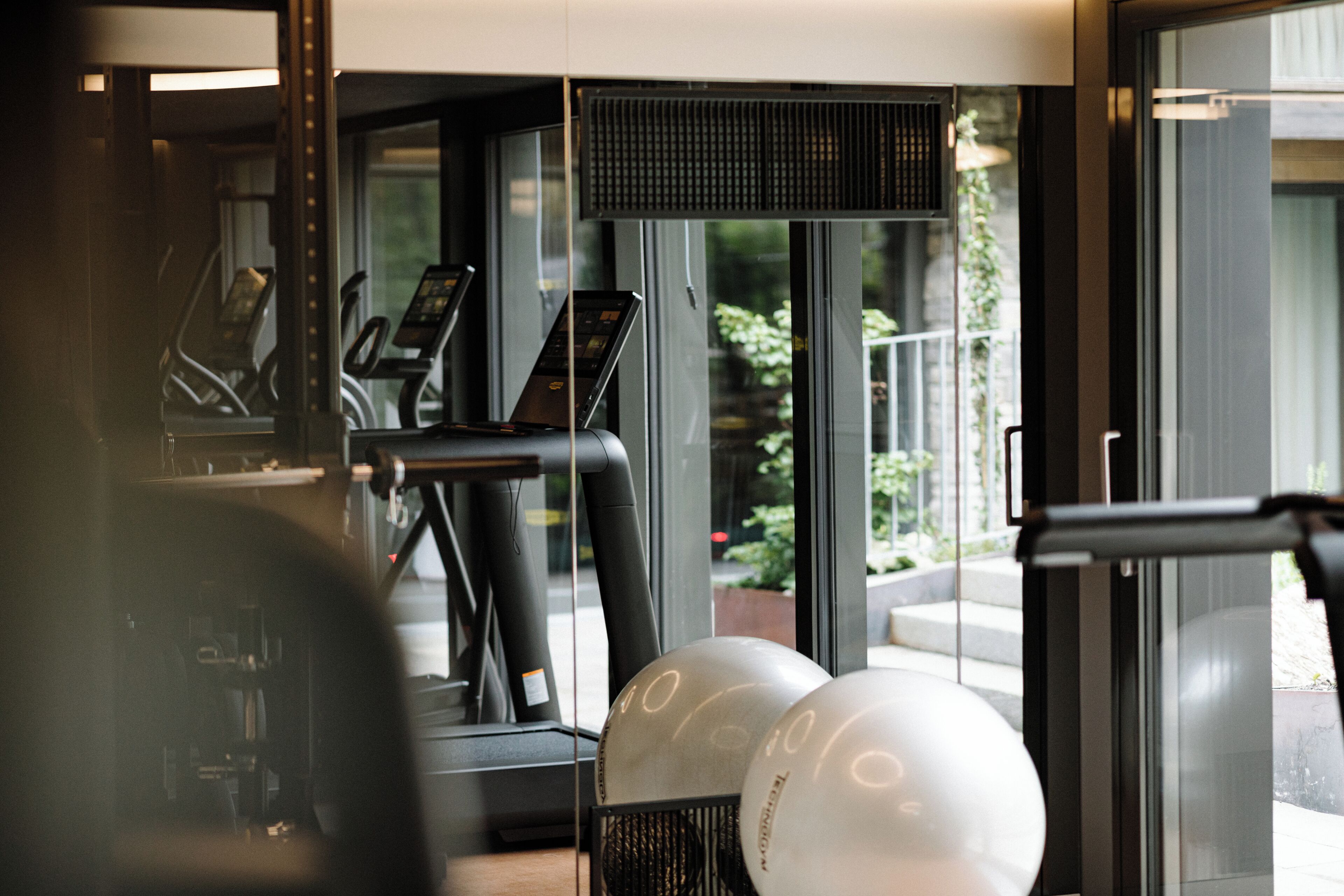 Un gimnasio con equipamiento de ejercicio y vistas al exterior a través de amplias ventanas.