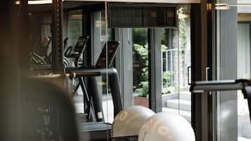 Un gimnasio con equipamiento de ejercicio y vistas al exterior a través de amplias ventanas.