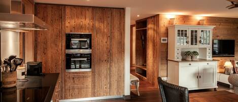 A modern kitchen with wooden paneling, built-in ovens, and a white cabinet with glass doors.