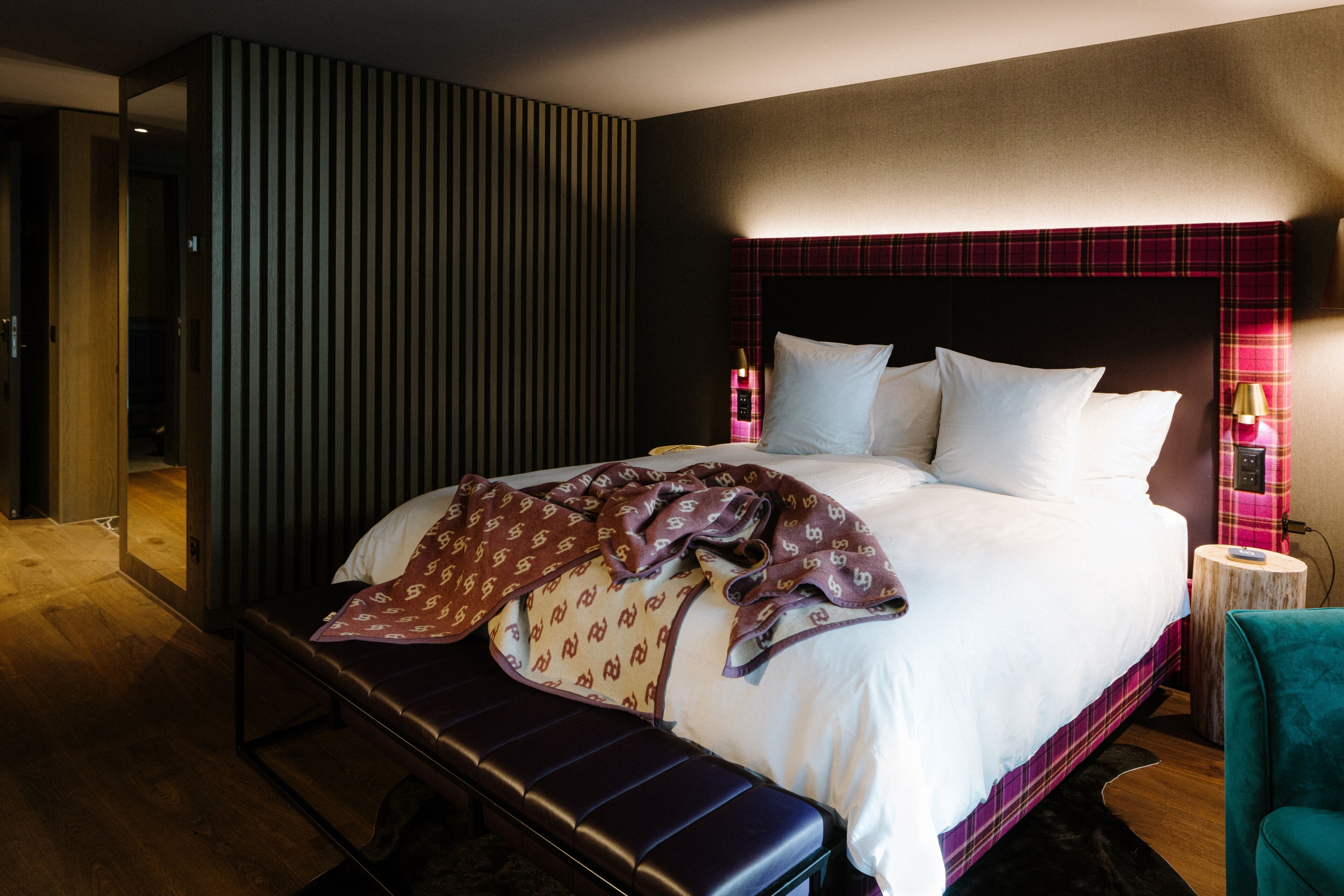 Una habitación de hotel moderna con una cama grande, un banco y una pequeña mesa con una lámpara.