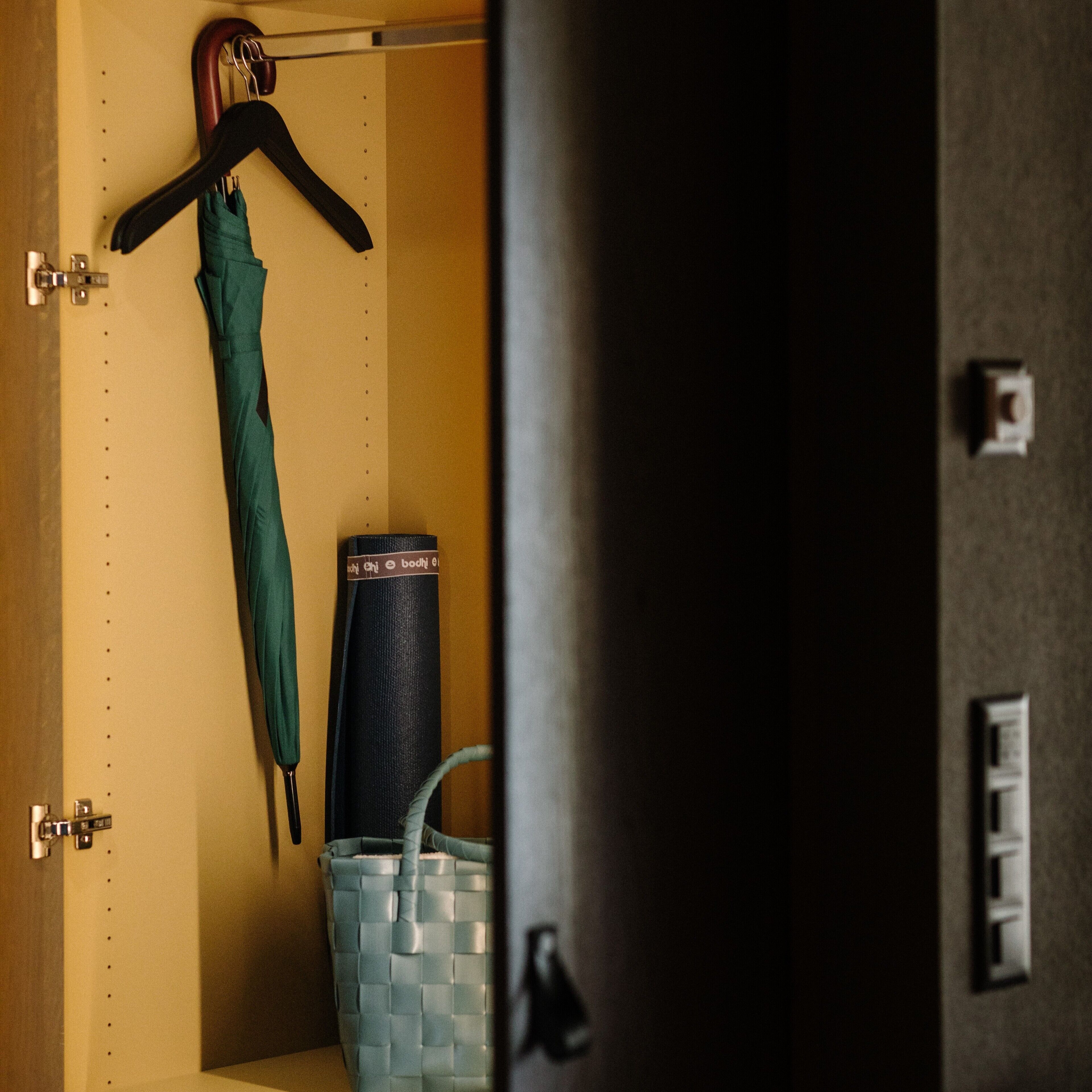 A room with a hanging rack, a blue woven bag, and a black cylindrical object.