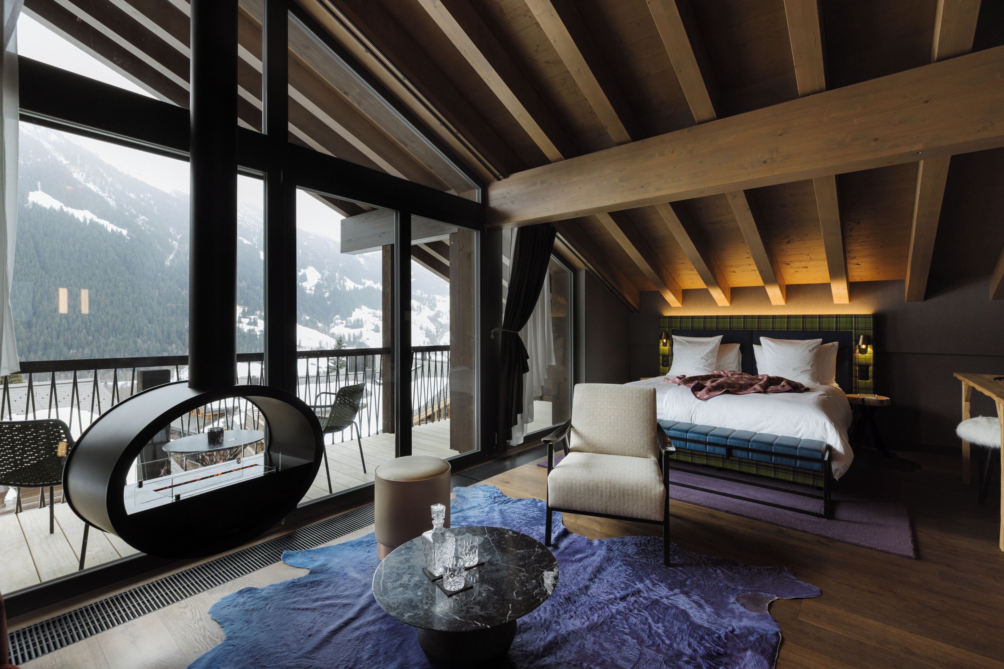 Habitación de hotel moderna con un ventanal grande, una cama, zona de estar y vistas a las montañas.