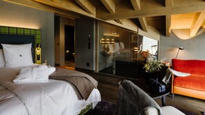A modern hotel room with a large bed, a sofa, a mirror, and a glass partition.