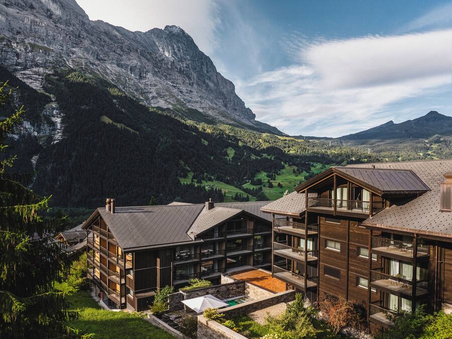 A mountain lodge with multiple wooden buildings, balconies, and a view of the surrounding mountains.