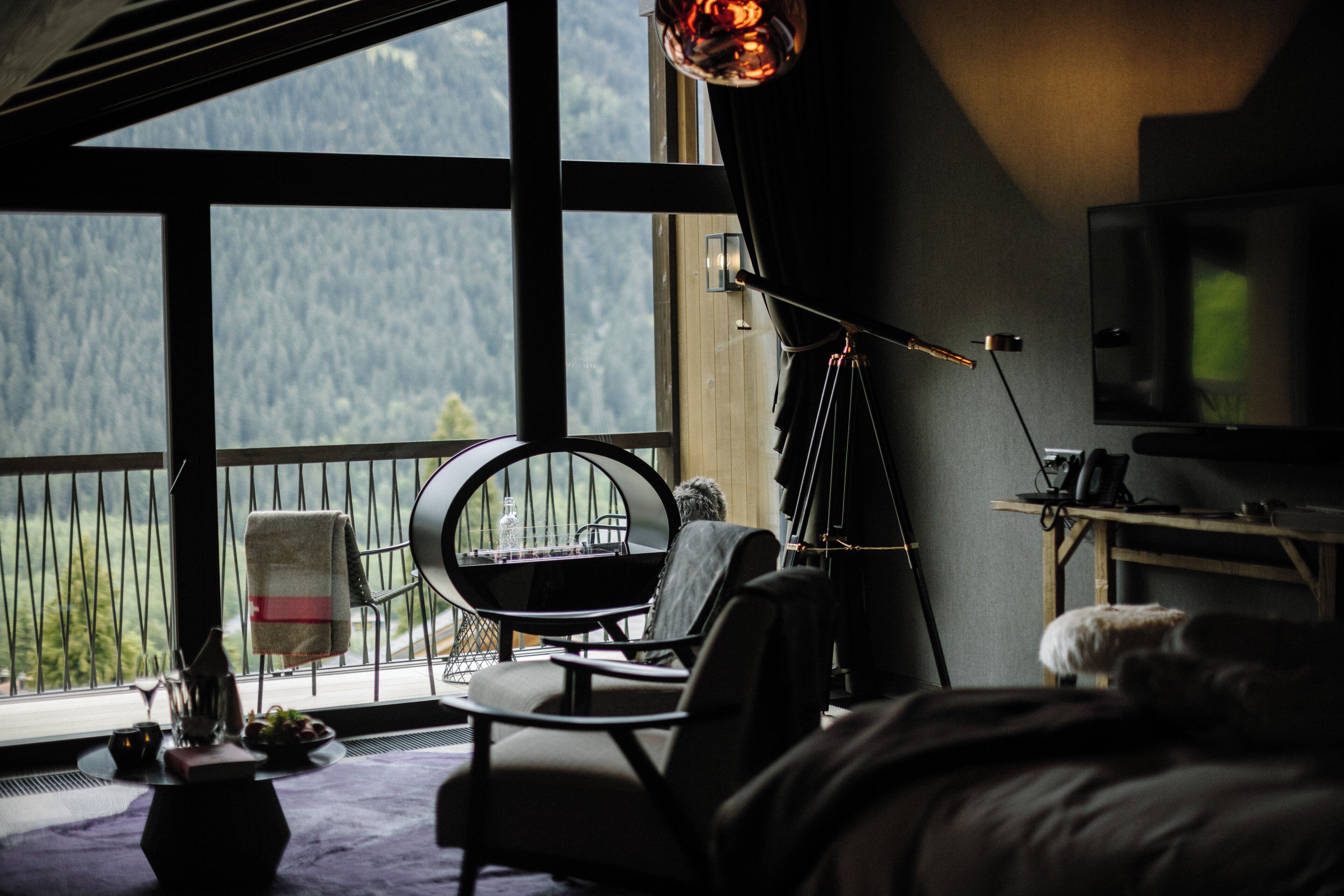 A room with a large window, a round table, a chair, a bed, and a television.