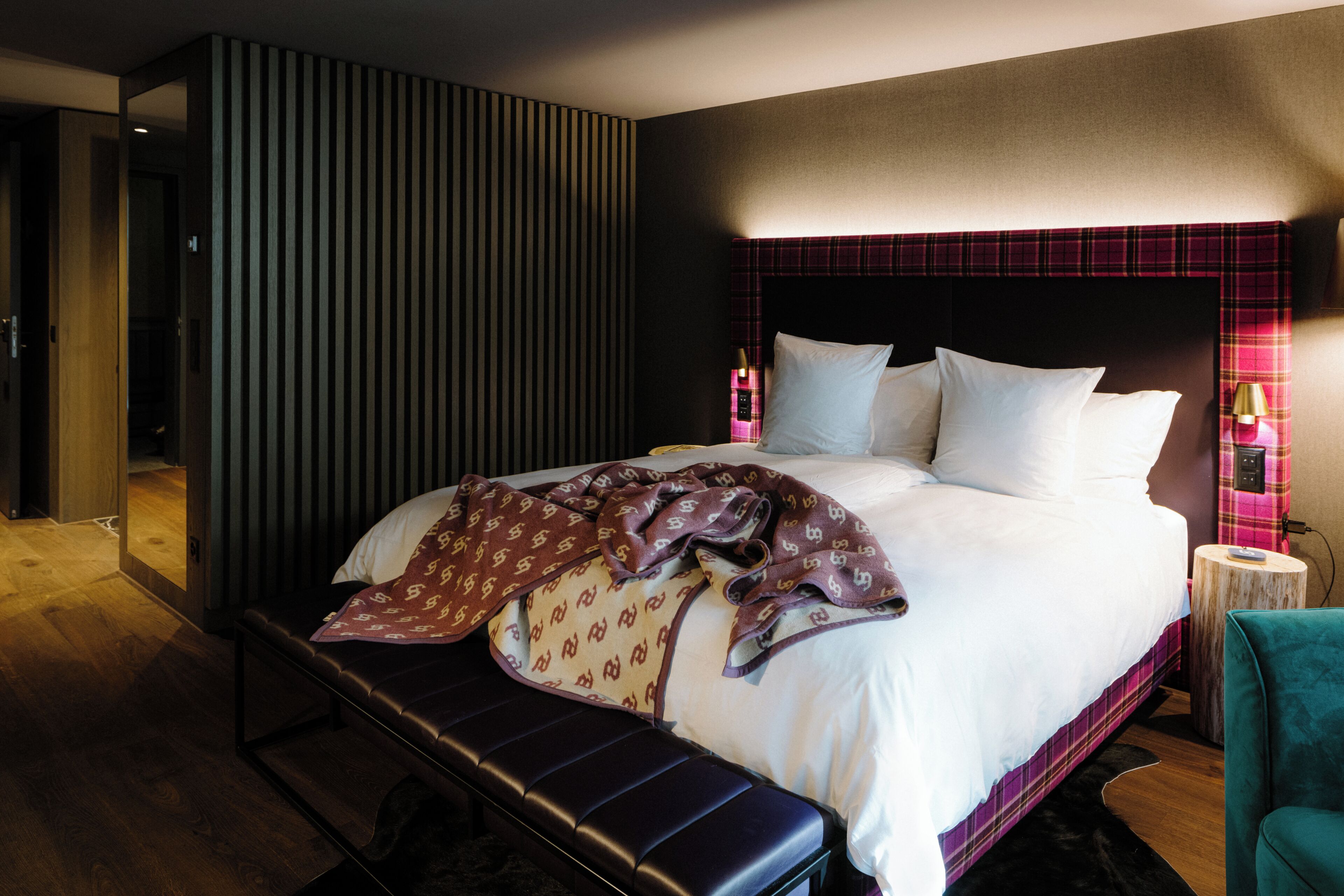 Una habitación de hotel moderna con una cama grande, un banco y una mesita de noche con una lámpara.