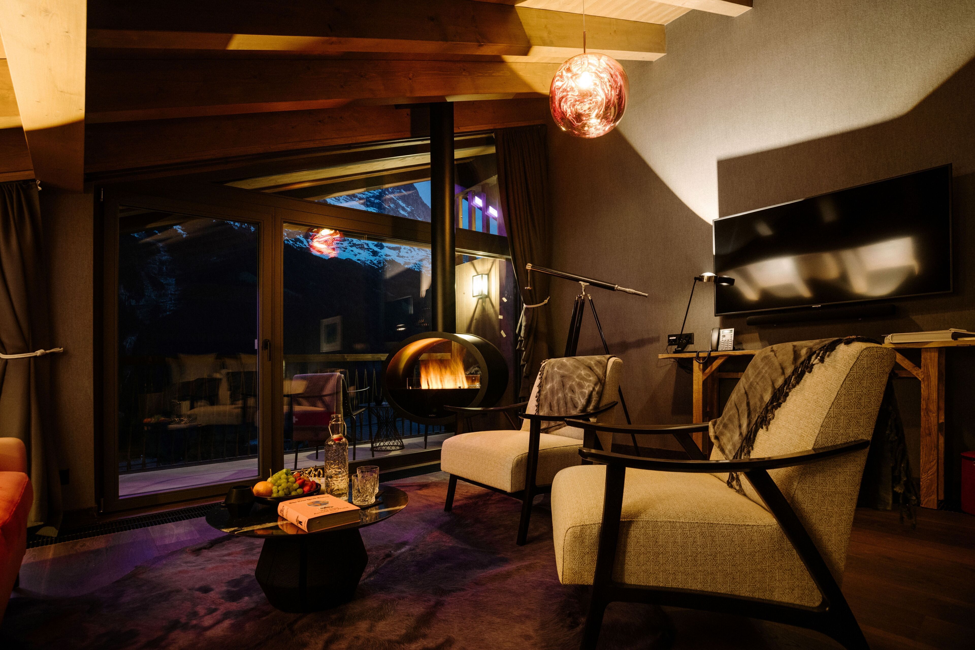 A modern living room with a fireplace, comfortable seating, a flat-screen TV, and a large window offering a view of the outdoors.