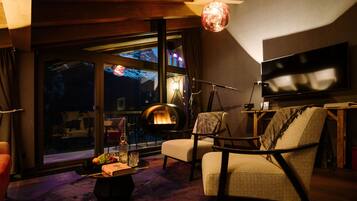 A modern living room with a fireplace, comfortable seating, a flat-screen TV, and a large window offering a view of the outdoors.