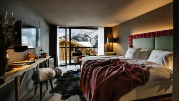 A modern hotel room with a large bed, a desk with a chair, a TV mounted on the wall, and a view of a mountain through a sliding door.