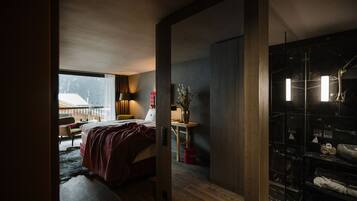 A modern bedroom with a large bed, a desk, and a bathroom with a glass shower.