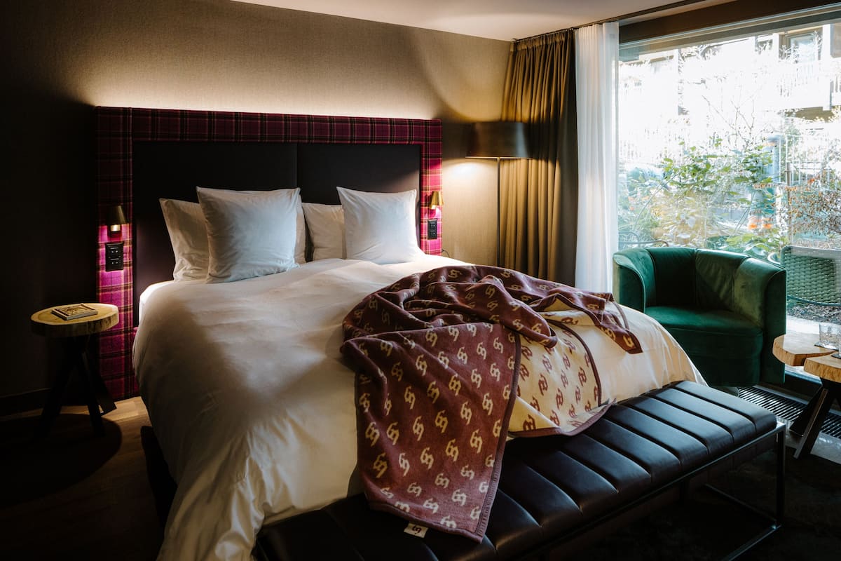 Una habitación de hotel con una cama grande, un sillón verde y una mesita.