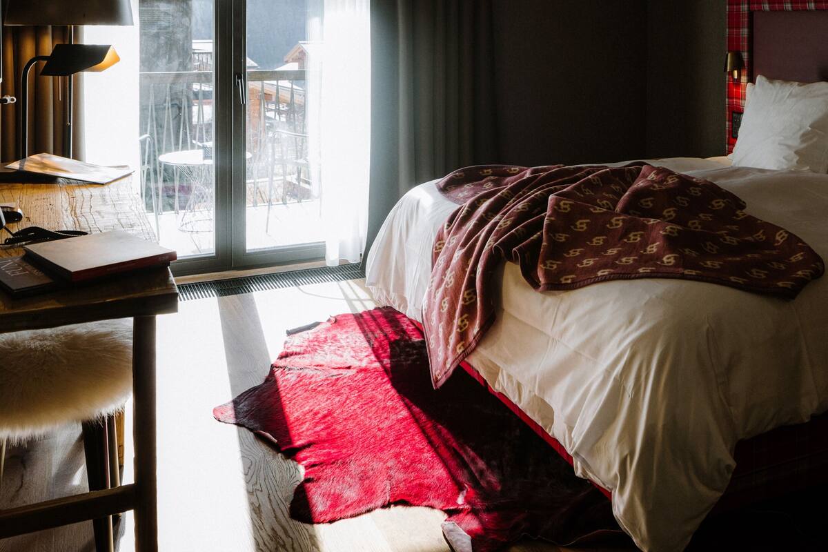 Habitación de hotel con cama, escritorio con lámpara y vistas al exterior.