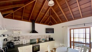 A kitchen with white cabinets, a black countertop, a built-in oven, and a dining area with a round table and white chairs. - Casa Albillo, Spanien (Puntagorda)