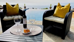 Two wicker chairs with yellow cushions, a bottle of Altitud Palomar 473 wine, two wine glasses, and a plate of snacks on a table with a view of the sea. - Casa Albillo, Spanien (Puntagorda)