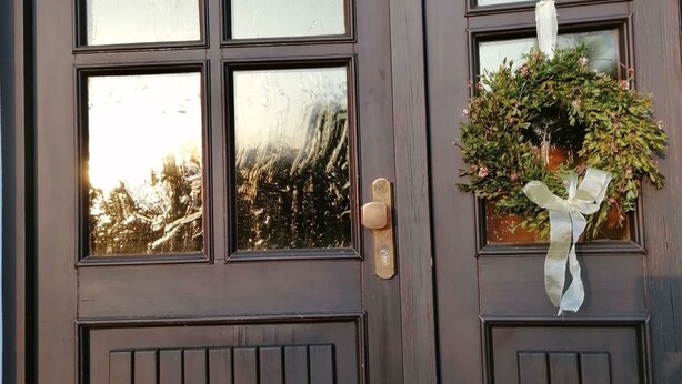 Una porta de fusta fosca amb quatre finestrals de vidre i una planta en test amb un llaç.