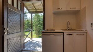 Uma cozinha compacta com lava-louças embutida, pia e armários superiores. Uma porta de madeira com um número é visível, e uma área externa coberta pode ser vista pela porta.
