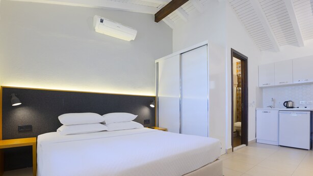Quarto de hotel moderno com uma cama grande, mesas de cabeceira, um guarda-roupa e uma kitchenette.