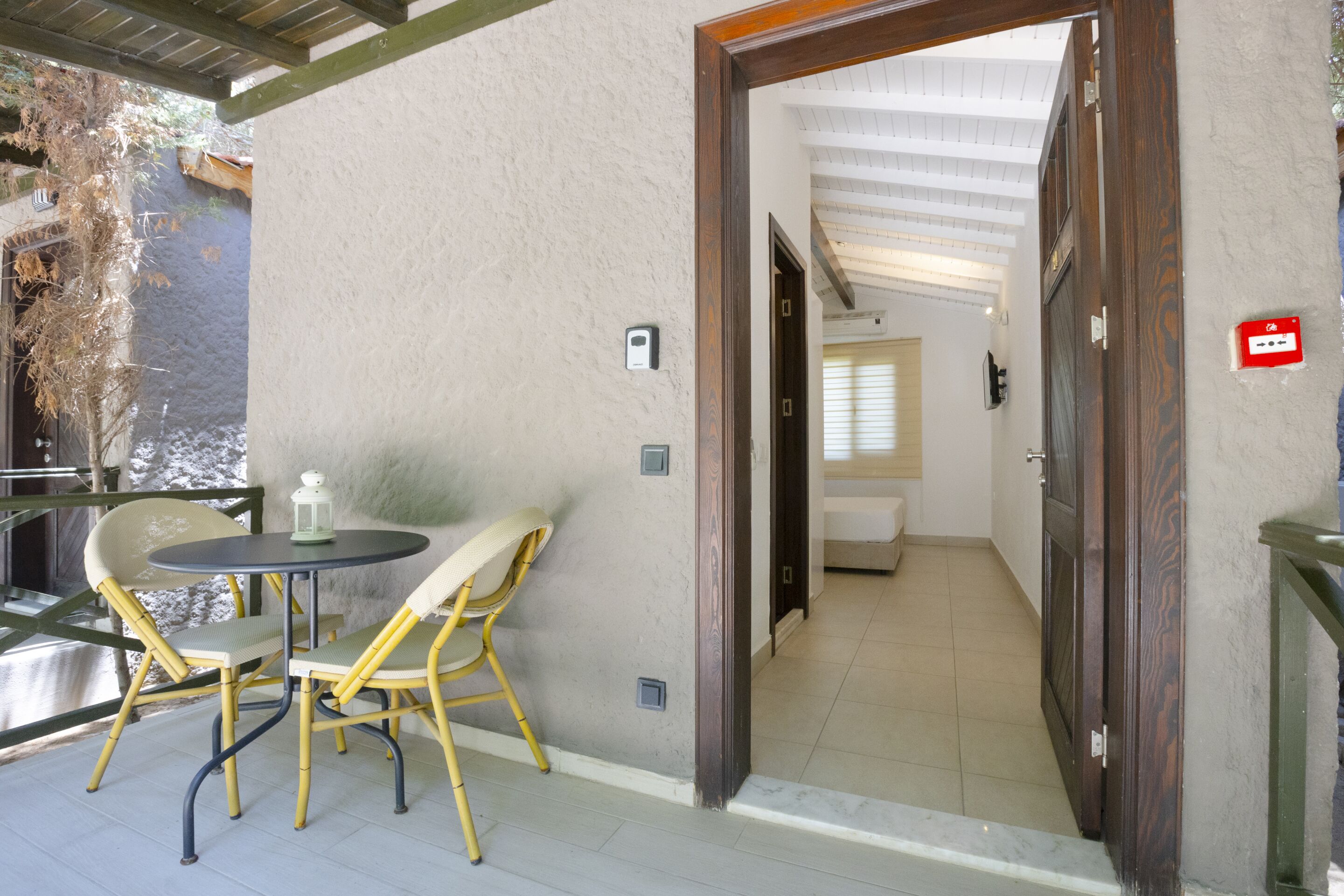 Une pièce avec une porte en bois, une petite table entourée de chaises et une vue sur un balcon doté d’une balustrade.