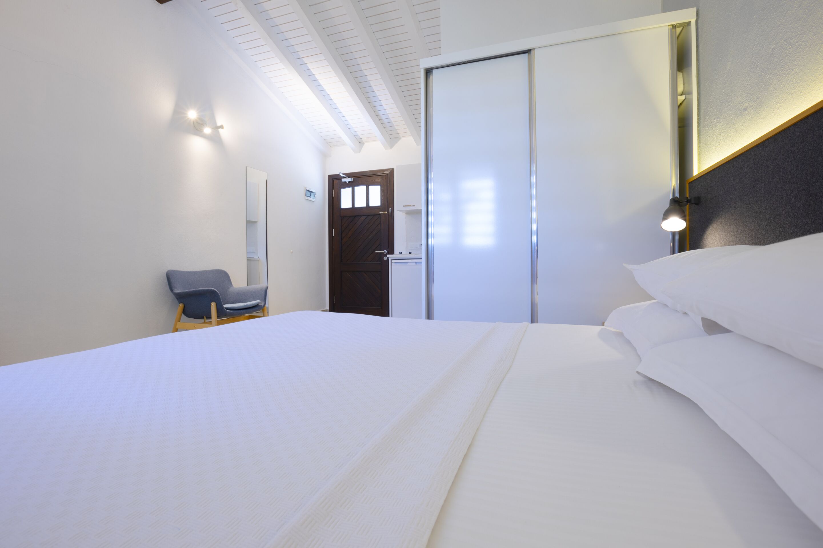 Une chambre d’hôtel moderne, dotée d’un grand lit, d’une chaise, d’une armoire et d’un miroir.