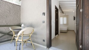 Um espaço ao ar livre pequeno e fechado, com uma mesa, cadeiras, uma porta que dá para um quarto e uma parede com textura.