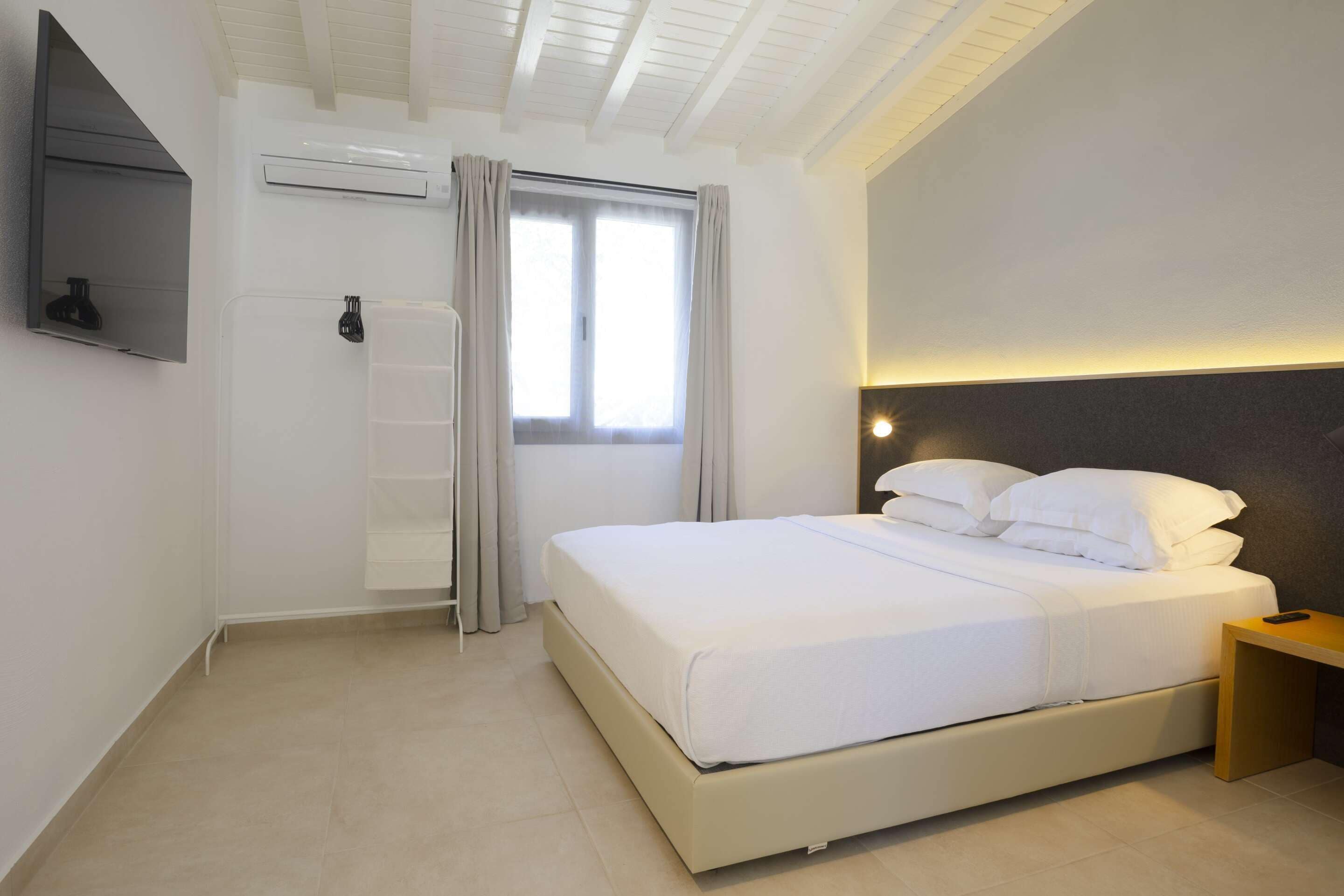 Une chambre d’hôtel moderne dotée d’un grand lit, d’un téléviseur à écran plat fixé au mur, d’un système de climatisation et d’une fenêtre avec des rideaux.