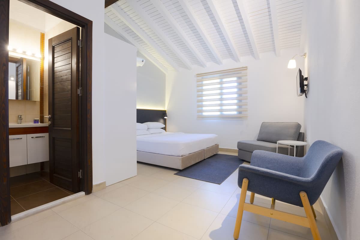 Un dormitorio moderno con cama, una silla, una mesita y una ventana con persianas.
