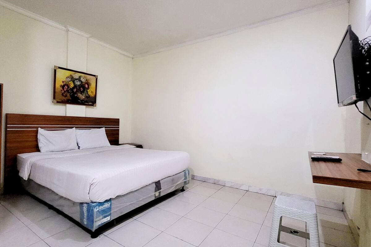 A bedroom with a wooden bed, a painting on the wall, and a TV mounted on the wall.