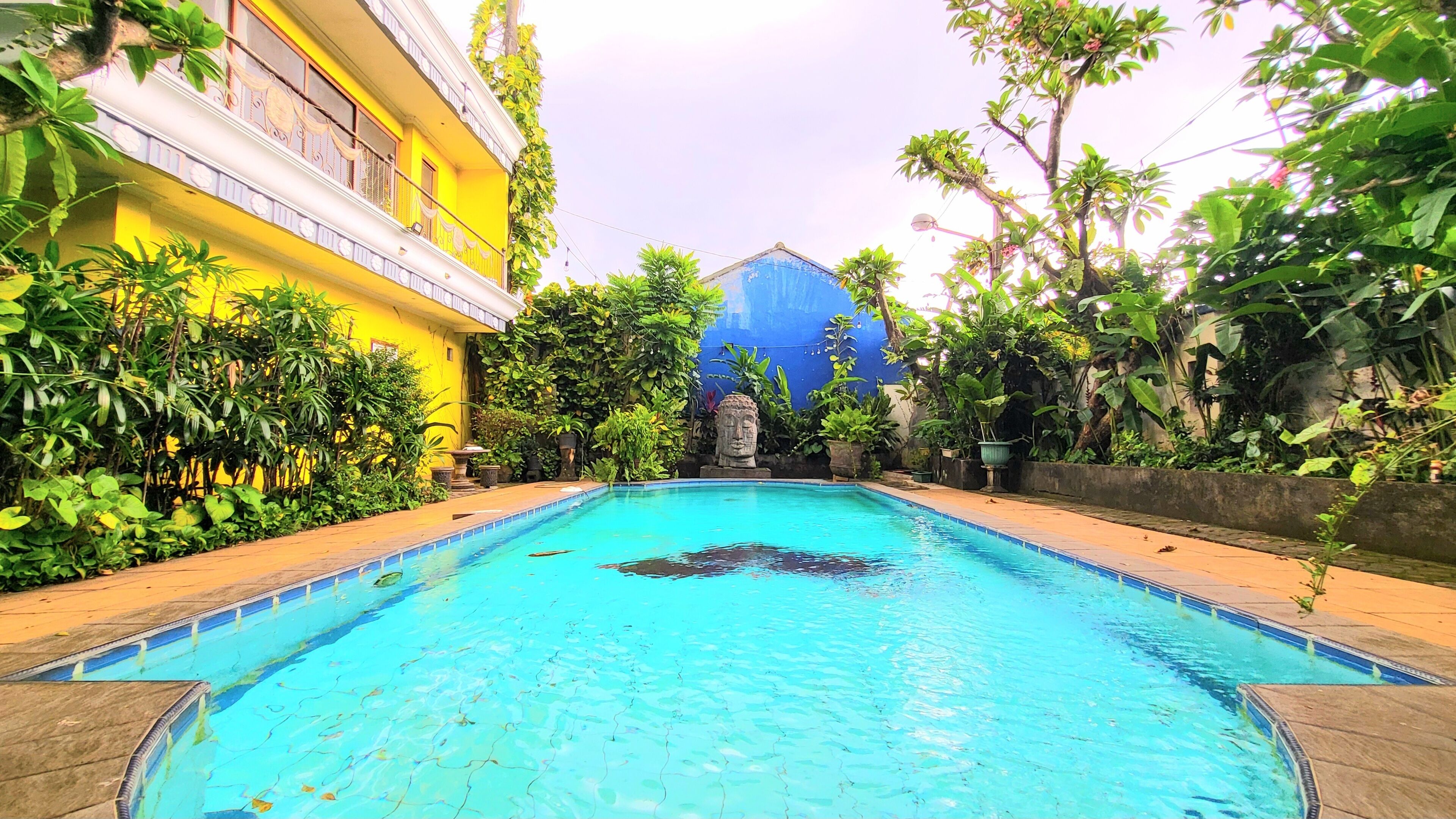 A swimming pool surrounded by lush greenery and a yellow building with balconies.
