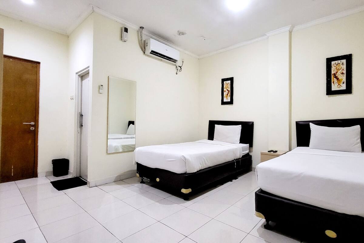 A hotel room with two beds, a mirror, an air conditioning unit, and a door.
