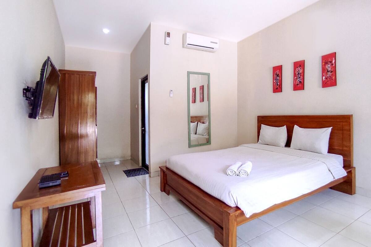 A hotel room with a bed, a desk, a mirror, and a shower.