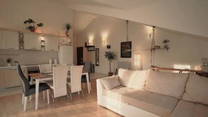 Una cocina moderna con armarios blancos, una mesa de comedor con sillas y un sofá blanco en la sala.